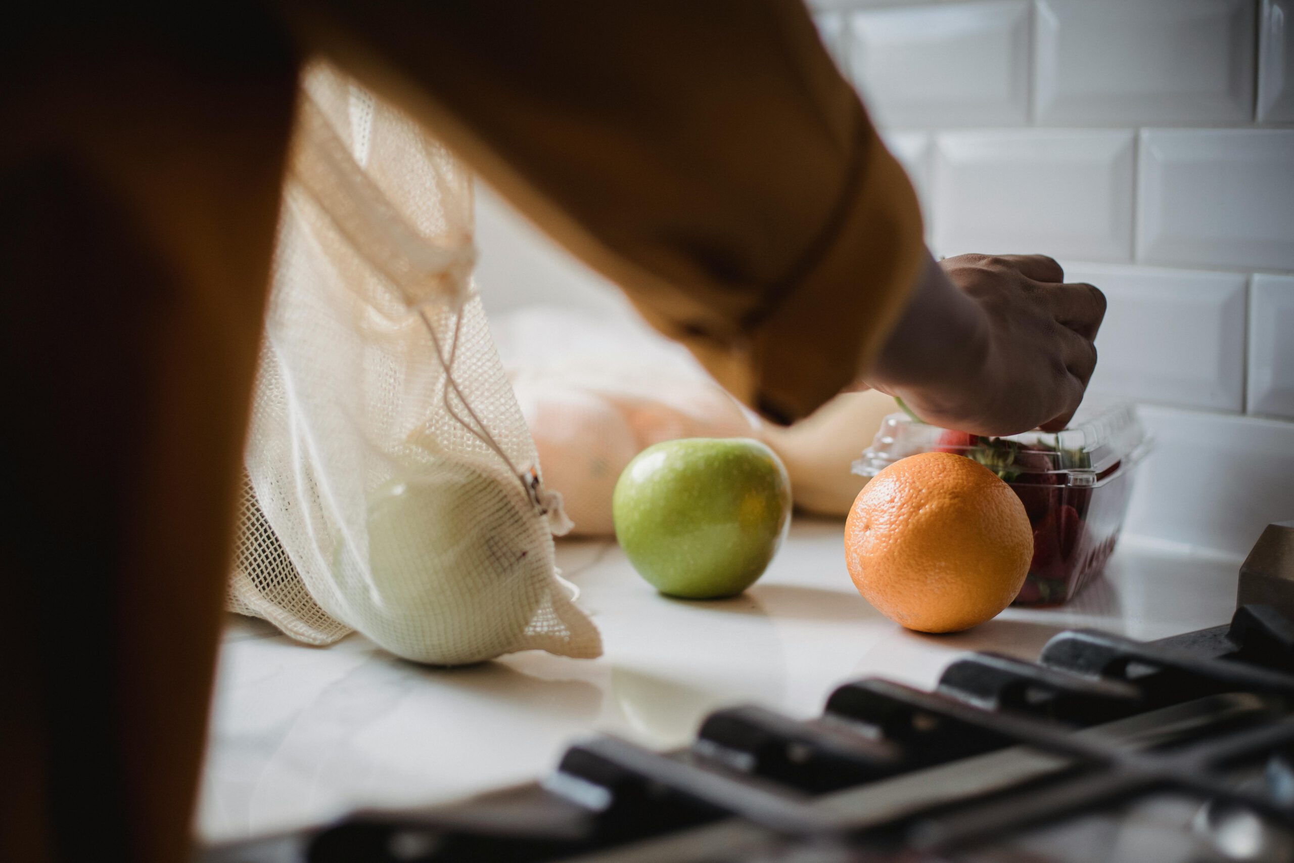 Person unpacking eco-friendly bag with fresh fruits in a modern kitchen.